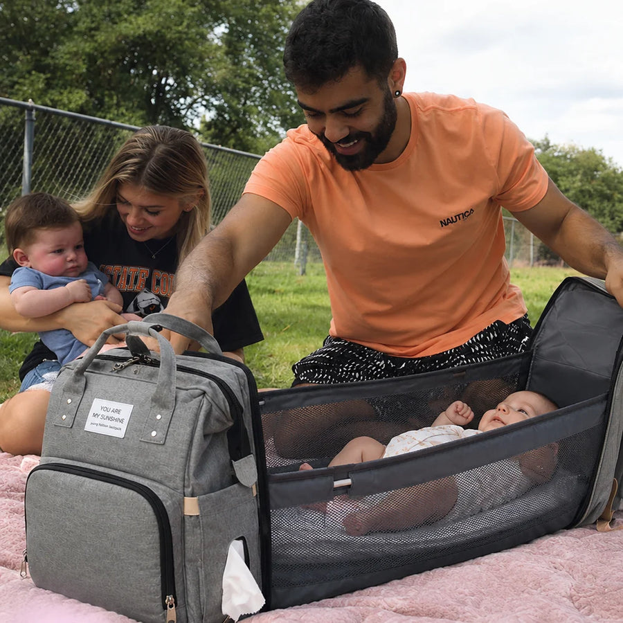 A dad unfolding the Cuddle Nest backpack's changing station on a picnic blanket