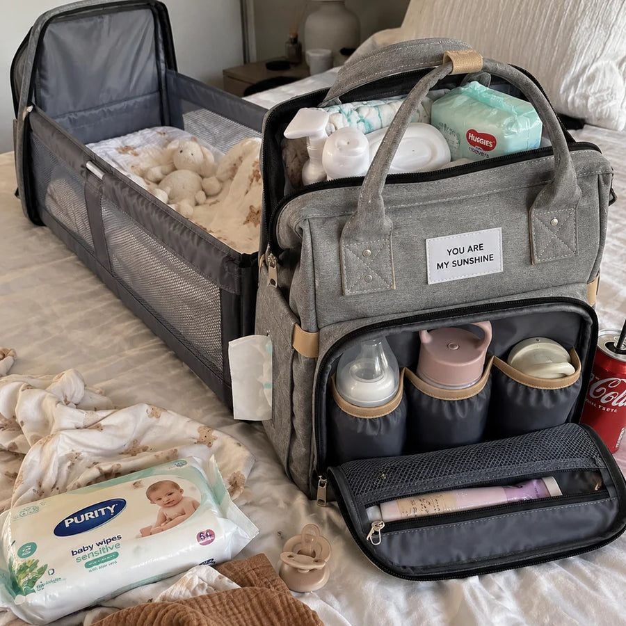 The packed Cuddle Nest backpack on a bed with bottles, nappies and wipes in their own pockets