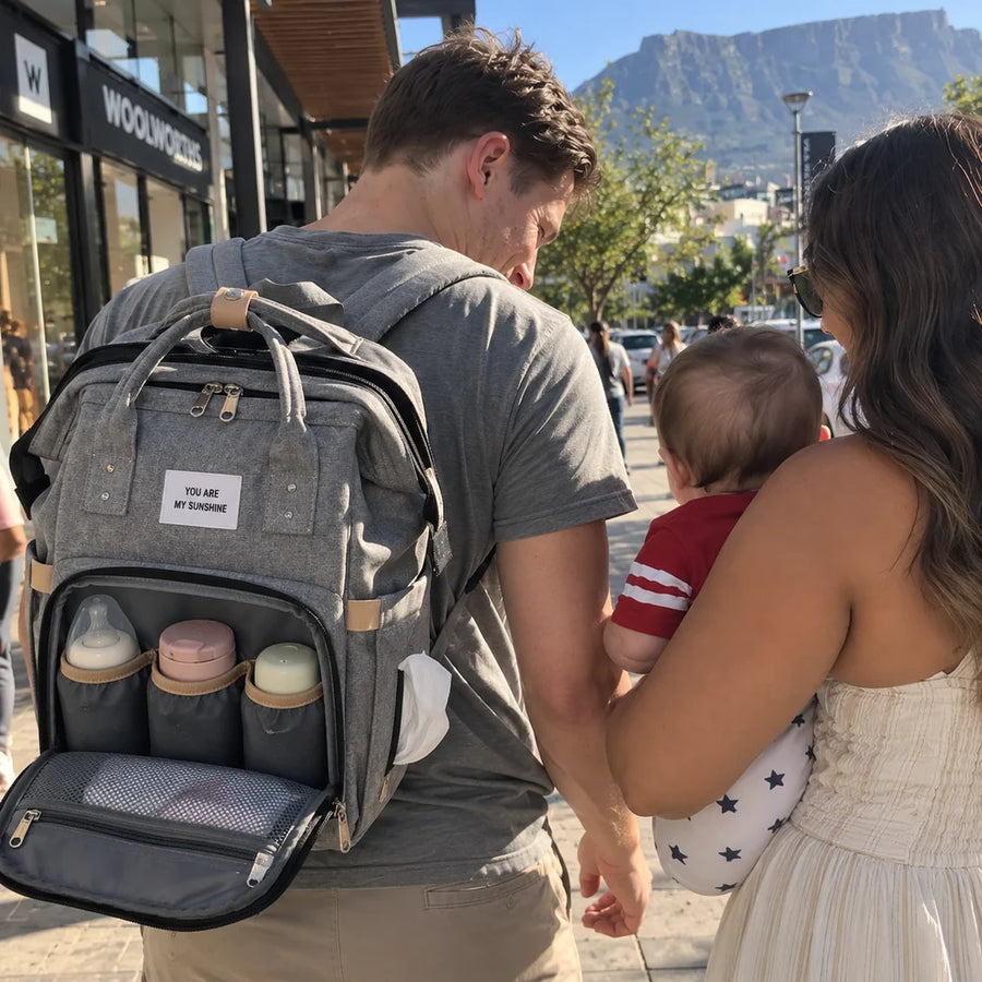 A dad wearing the Cuddle Nest backpack at the V&A Waterfront, front pocket open with three bottles