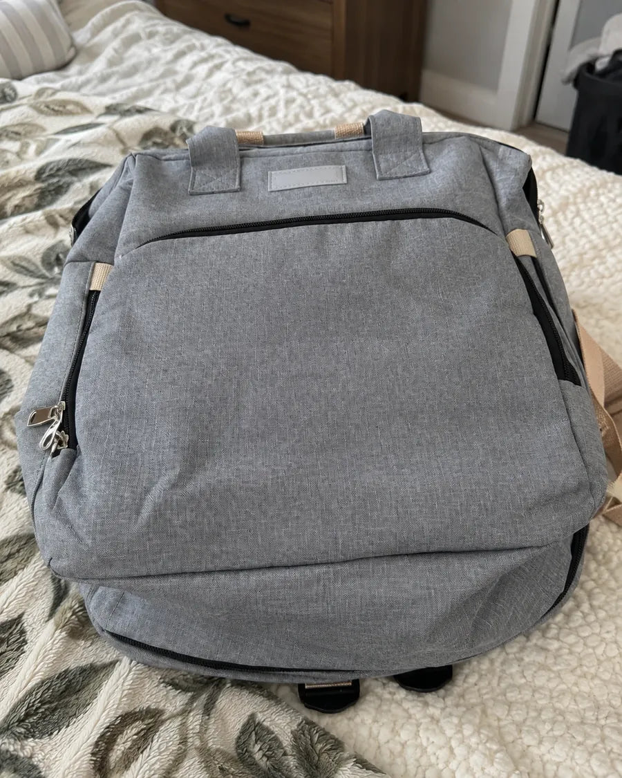 Buyer's photo: the front of the grey backpack on a bed