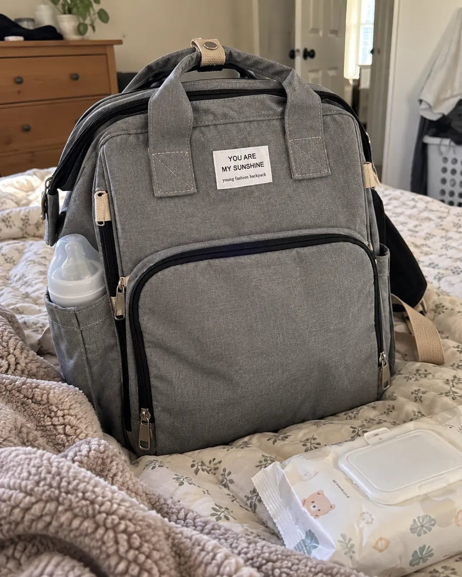 Buyer's photo: the grey backpack on a bed with a bottle in the side pocket and a pack of wipes